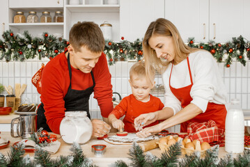 Friendly family making cookies shapes in raw flat dough on a kitchen table using a cookie cutter to...