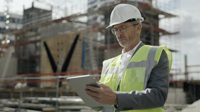 Aged man in helmet working on tablet on construction site