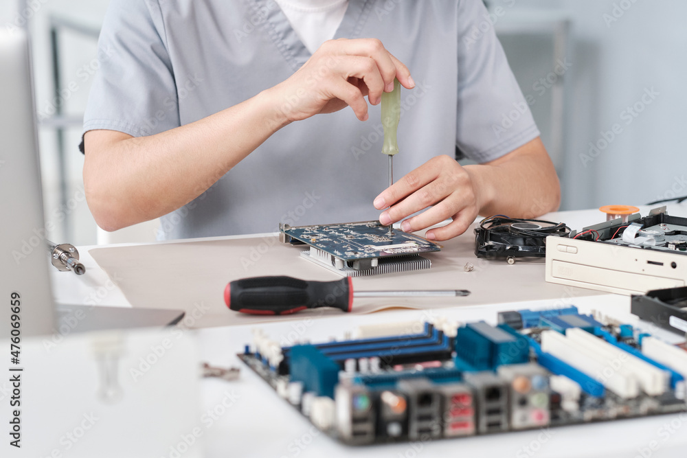 Poster hands of young repairperson in uniform fixing details of circuit board with screwdriver while sittin