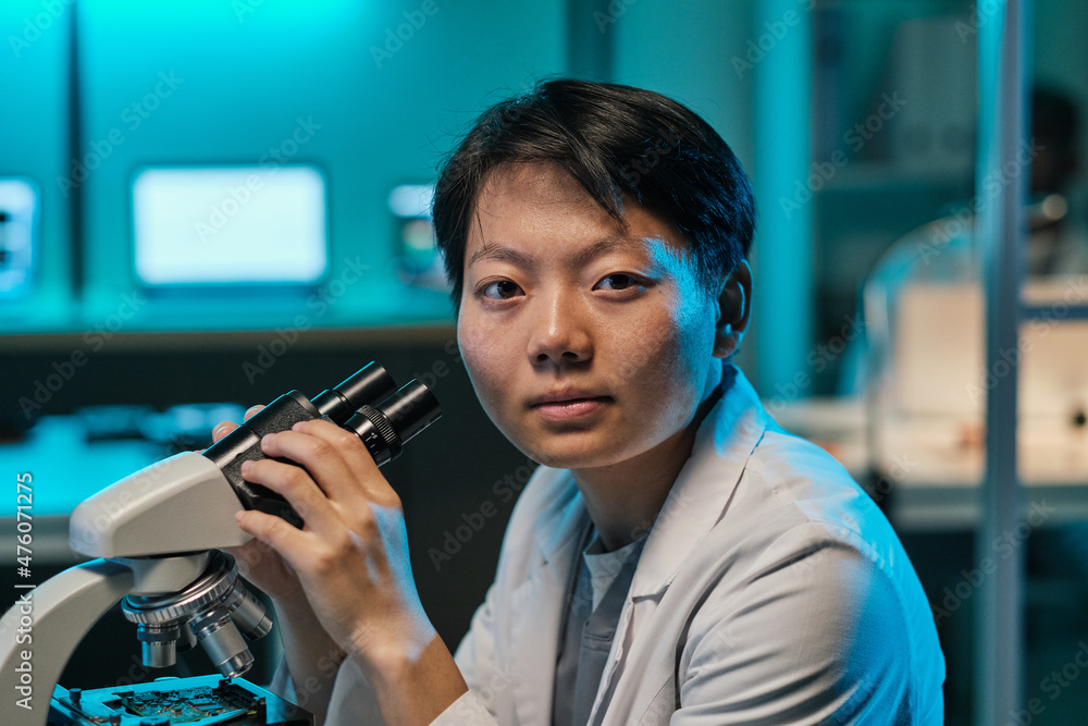 Aufkleber young confident female scientist or technician with microscope looking at you while sitting by workp