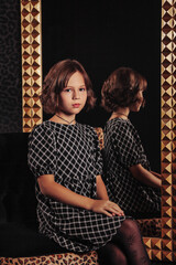 Portrait of pretty cute teenager girl in an elegant dress at mirror
