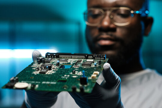 Circuit board in gloved hands of young contemporary African laboratory worker holding it in front of camera