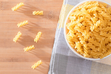 Uncooked Fusilli Pasta in White Bowl on Wooden Board. Raw and Dry Macaroni. Unhealthy and Fat Food. Italian Culture