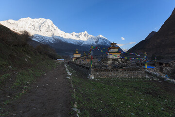 Buddhist monastery in the Sama valley at the foot of sunlighted snow-covered mountain peak - obrazy, fototapety, plakaty