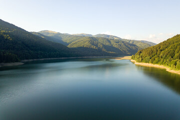 Aerial view of big lake with clear blue water between high mountain hills covered with dense evergreen forest.