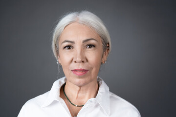 Portrait of senior woman with white hair in white blouse looking at camera isolated on grey...