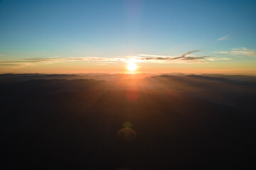 Aerial view of dark mountain hills with bright sunrays of setting sun at sunset. Hazy peaks and misty valleys in evening