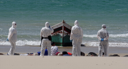 Illegal migrants at the coast of Cadiz, Spain, guarded by the police in protective suits.