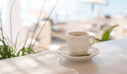 A white cup of coffee on the terrace in cafe on the beach on a summer sunny day. Close-up. Copy space.