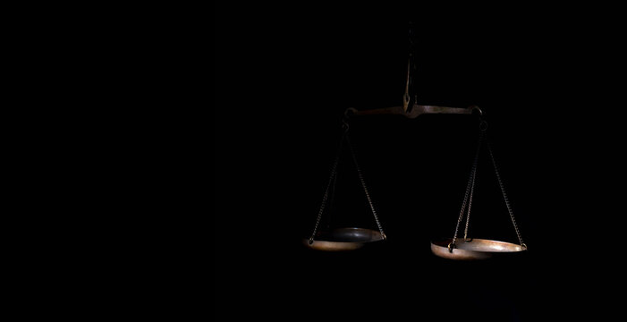 Scales of justice on simple black background. Selective focus on right rart of weight. Copy space.