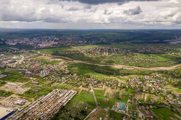 Fototapeta premium Aerial view of town or village with rows of buildings and curvy streets between green fields in summer. Countryside landscape from above.