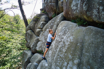 Determined boy climber clambering up steep wall of rocky mountain. Child overcoming difficult route. Engaging in extreme sports and rock climbing hobby concept