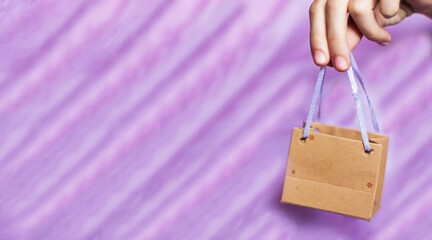 Close-up of a girl holding in her hand a small blank paper gift bag on a purple background. Packaging template mock up. Delivery concept advertising mockup