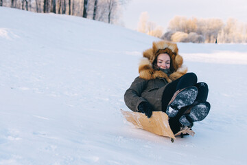 Young woman sliding downhill on piece of paperboard in park.