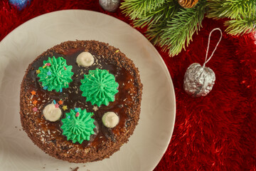 Сhocolate cake decorated with Christmas trees, festive painted walnuts  and a  fir branch on a red background