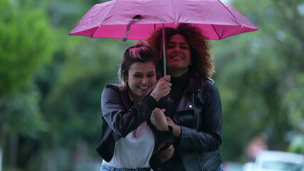 Two friends together during rainy day, person opening umbrella covering friend in rain in street