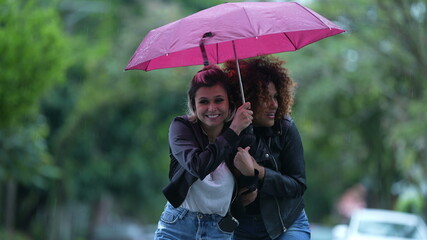 Two friends together during rainy day, person opening umbrella covering friend in rain in street