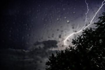 Raindrops on window glass and lightning in the background.