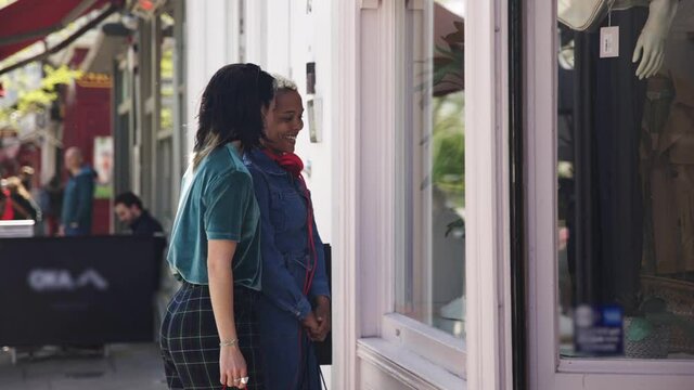 Lesbian couple standing in front of store window shopping in the city