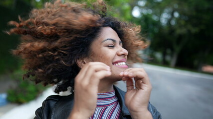 Fototapeta na wymiar Carefree black woman playing with curly hair outside in street