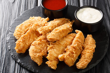Breaded chicken strips with two kinds of sauces on a Board. Fast food on black background. Horizontal