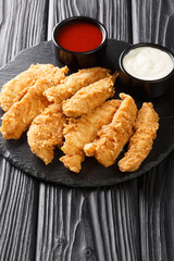 Breaded chicken strips with two kinds of sauces on a black board on the table. Vertical