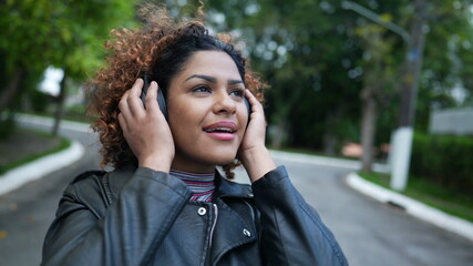 Carefree black woman dancing to music outside in street wearing headphones