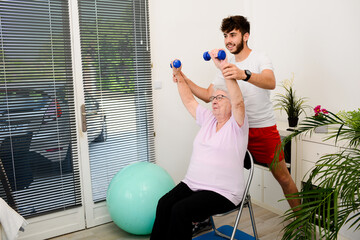 senior elderly woman with a personal trainer private fitness coach at home handsome young man