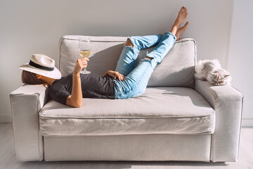 Young woman with glass of white wine resting on the sofa at home. Woman enjoying free time and lazy weekend.