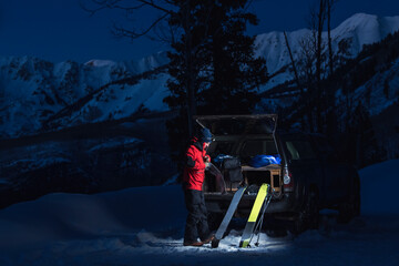 Man with splitboards standing by truck in snow