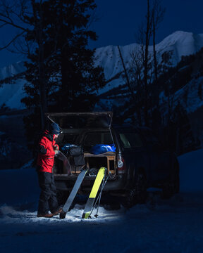 Man with splitboards standing by truck in snow at dusk