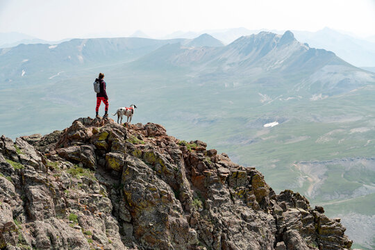 Female hiker standing on mountain peak with dog on sunny day
