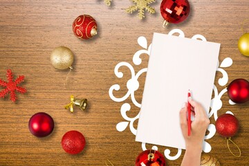 Woman's hand writes a list of goals for the new year. Christmas composition with a blank white sheet, Christmas tree toy, and garland.