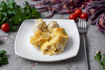 A hearty lunch for the whole family: cauliflower baked with cheese in cream sauce on a white plate on a gray background. Close-up