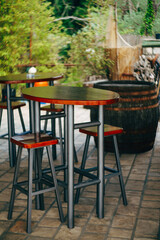 Fototapeta na wymiar High metal table with wooden top and low stools in a street cafe