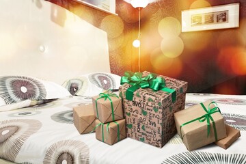 Boxes with Christmas gifts on the bed with a blanket and pillow. The bedroom is decorated with Christmas lights.