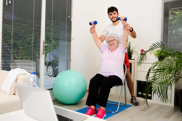 senior elderly woman with a personal trainer private fitness coach at home handsome young man