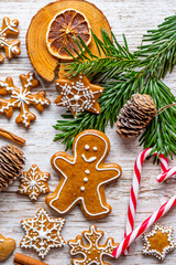 Christmas gingerbread and sweets are placed on wooden desk. Cookies and sweet food in shape of stars and snow flakes. Winter theme, rustic style. Pine trees on the side. Candy stick and other spice.