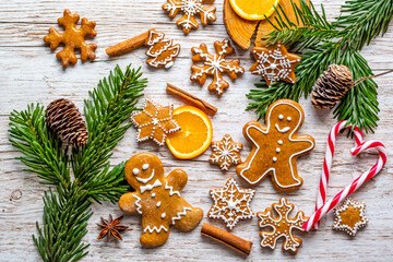 Christmas gingerbread and sweets are placed on wooden desk. Cookies and sweet food in shape of stars and snow flakes. Winter theme, rustic style. Pine trees on the side. Candy stick and other spice.
