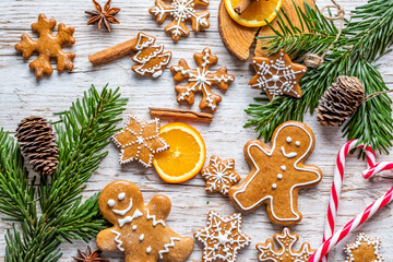 Christmas gingerbread and sweets are placed on wooden desk. Cookies and sweet food in shape of stars and snow flakes. Winter theme, rustic style. Pine trees on the side. Candy stick and other spice.