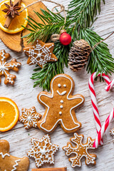 Christmas gingerbread and sweets are placed on wooden desk. Cookies and sweet food in shape of stars and snow flakes. Winter theme, rustic style. Pine trees on the side. Candy stick and other spice.