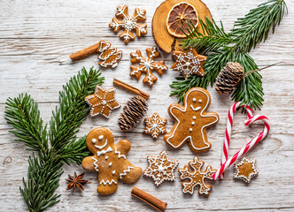 Christmas gingerbread and sweets are placed on wooden desk. Cookies and sweet food in shape of stars and snow flakes. Winter theme, rustic style. Pine trees on the side. Candy stick and other spice.