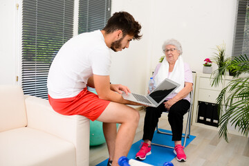 senior elderly woman with a personal trainer private fitness coach at home handsome young man