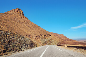 Asphalt road , small Atlas mountains and rock hills both sides, clear sky above - typical landscape in Southern Morocco