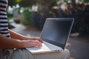 Obraz premium Female hands on laptop, woman types on keyboard sitting in park. Working outside and freelance concept, distance learning