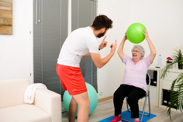 senior elderly woman with a personal trainer private fitness coach at home handsome young man