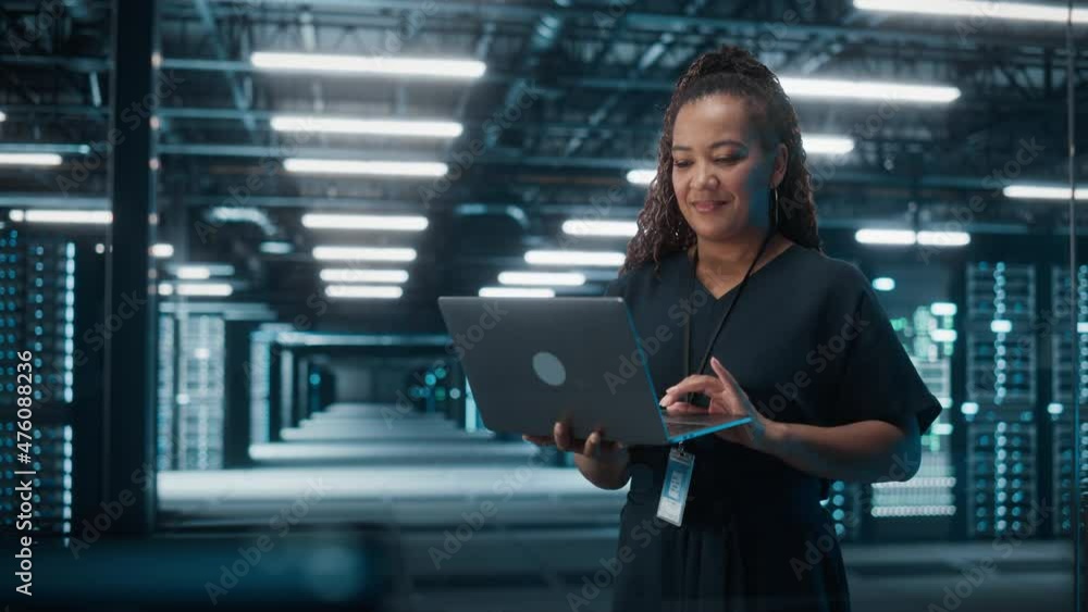 Poster Portrait of Successful African American Female IT Specialist Using Laptop, Standing in Data Center. System Administrator Works on Web Services. Cloud Computing, Server Analytics, Cyber Security