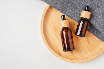 Obraz na płótnie Canvas Amber glass dropper bottles with bamboo lid on wooden plate for product presentation. Skincare cosmetic on grey fabric. Beauty concept for face body care