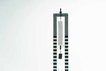 Weight hangs from a metal spring. Used for a vibration experiment or to determine the stiffness of the spring. Science experiment, used in physics class.