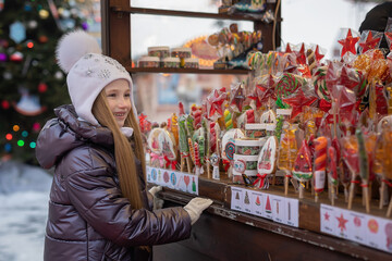 girl looks, chooses, buys caramel, lollipops, candies at the Christmas market